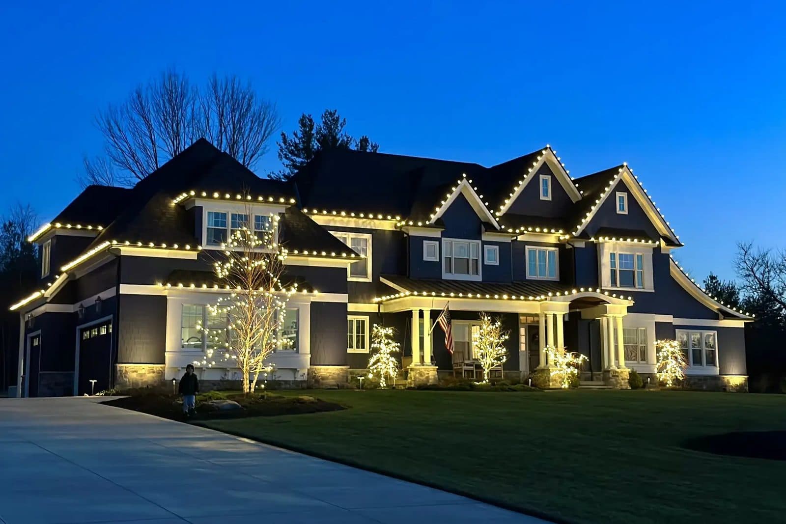 Two-story home outlined in warm-white Christmas lights at dusk